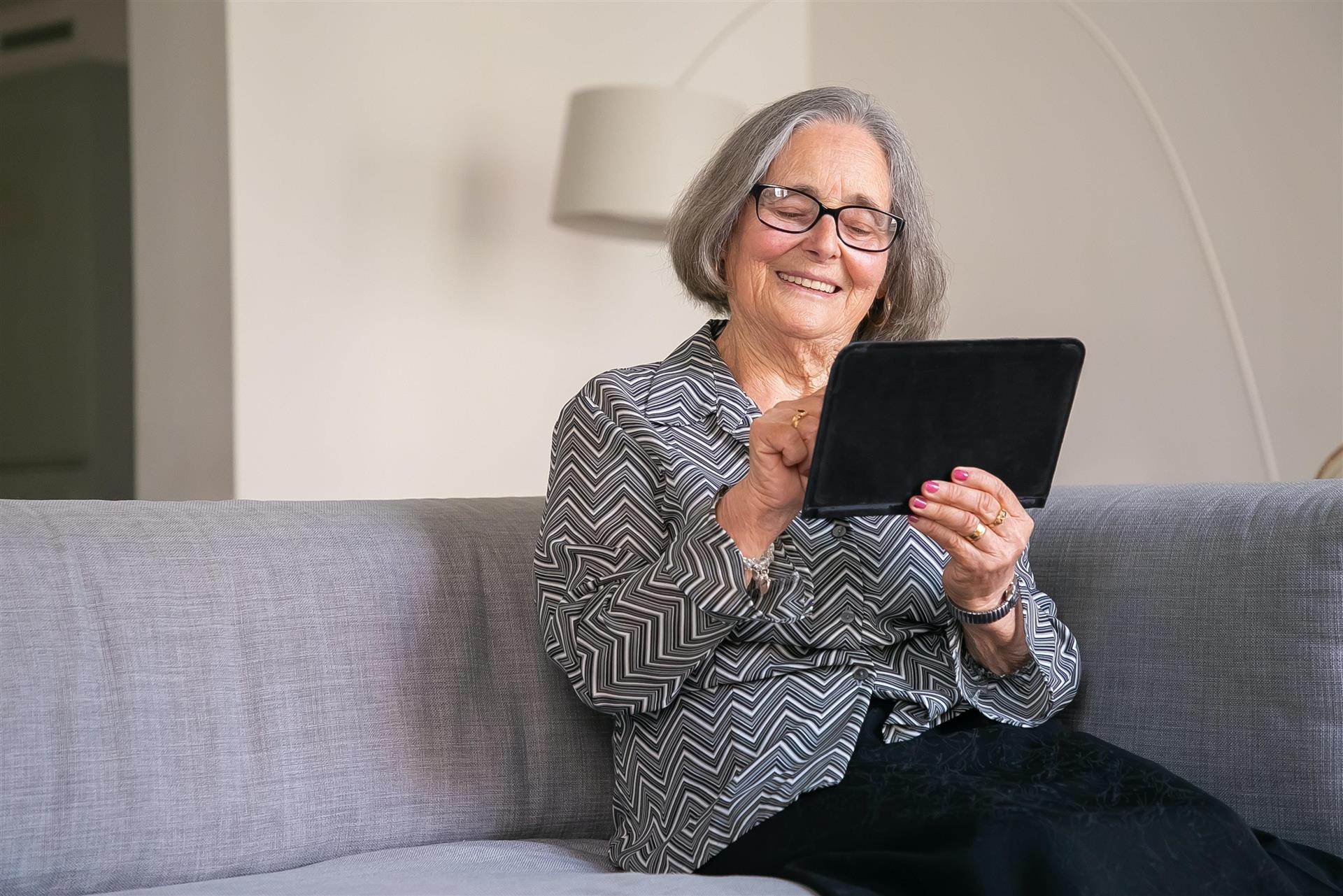Godt voksen dame sitter i sofaen og ser på ipad.
