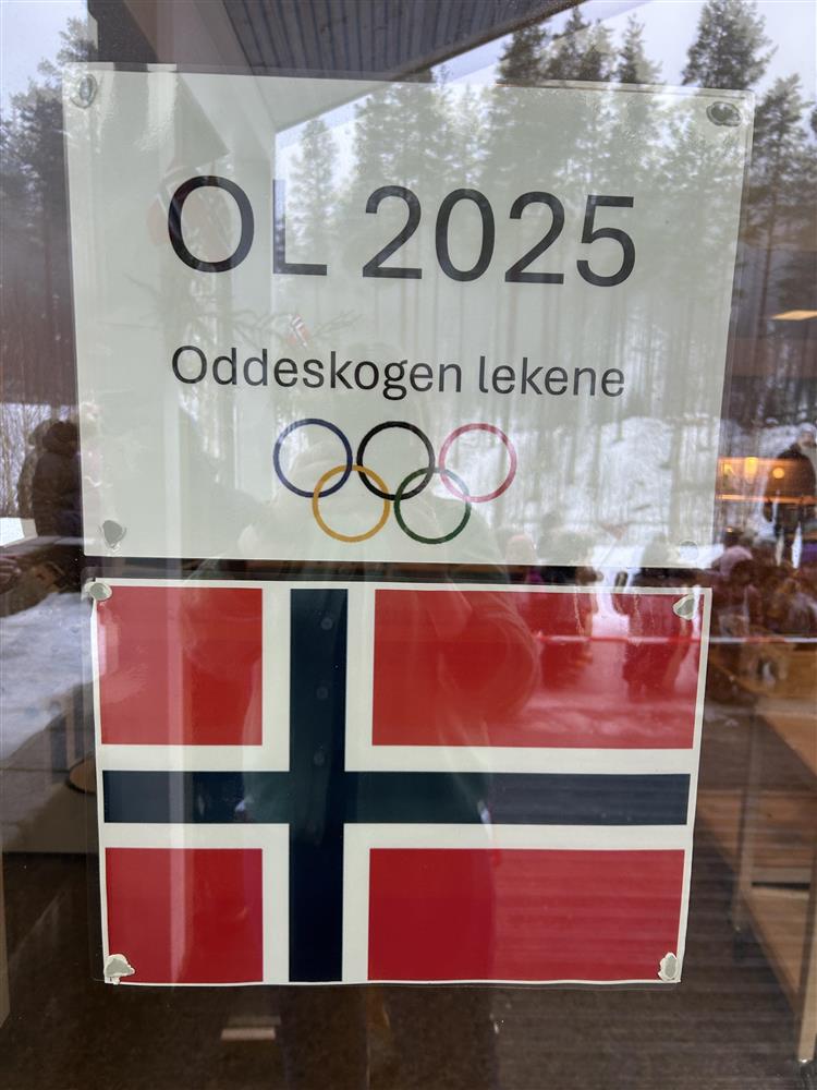 Bilde fra arrangementet "OL i Oddeskogen barnehage". Bildet viser plakater som henger på et vindu i barnehagen. Det er plakat av det norske flagget og teksten "OL 2025, Oddeskogenleikene" og viser de olympiske ringene. - Klikk for stort bilde